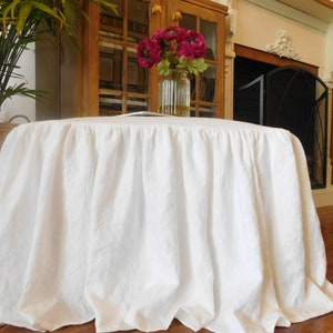 Puede incluir: Falda de mesa de lino blanco con un borde fruncido. La falda est&aacute; drapeada sobre una mesa redonda y est&aacute; en una habitaci&oacute;n con una chimenea y una librer&iacute;a.