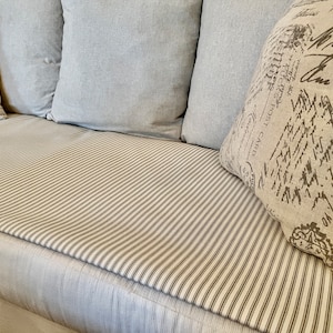 May include: A white couch with a striped cushion and three pillows. The pillows are made of a light gray fabric and have a white and black print.