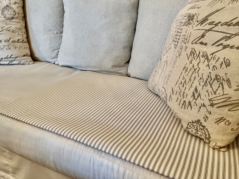 May include: A white couch with a striped cushion and three pillows. The pillows are made of a light gray fabric and have a white and black print.