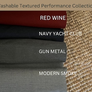 May include: Fabric swatches in shades of red wine, navy, gun metal, and modern smoke are displayed. The text reads "Washable Textured Performance Collection". The swatches are presented against a textured, neutral background.