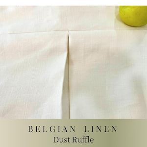 May include: A close-up of a white Belgian linen dust ruffle. The fabric is folded with a central pleat. The text "BELGIAN LINEN Dust Ruffle" is displayed at the bottom of the image. Two green apples are visible.