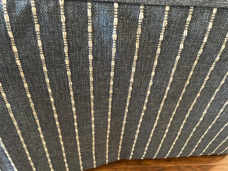 May include: Close-up of a textured fabric with a dark blue background and vertical white stripes. The stripes are evenly spaced and have a dotted pattern within them, creating a subtle, elegant design.