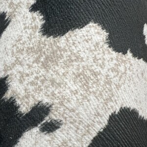 May include: Close-up of a black and white cowhide pattern. The pattern is made of a textured fabric with a fuzzy surface.