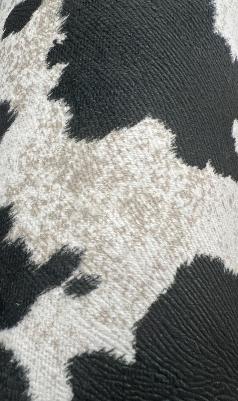 May include: Close-up of a black and white cowhide pattern. The pattern is made of a textured fabric with a fuzzy surface.