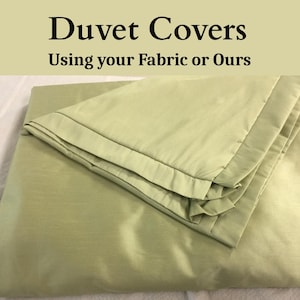 May include: A folded, light green duvet cover with a satin finish. The top of the duvet cover is folded over, revealing a contrasting border. Text at the top reads "Duvet Covers" and "Using your Fabric or Ours".