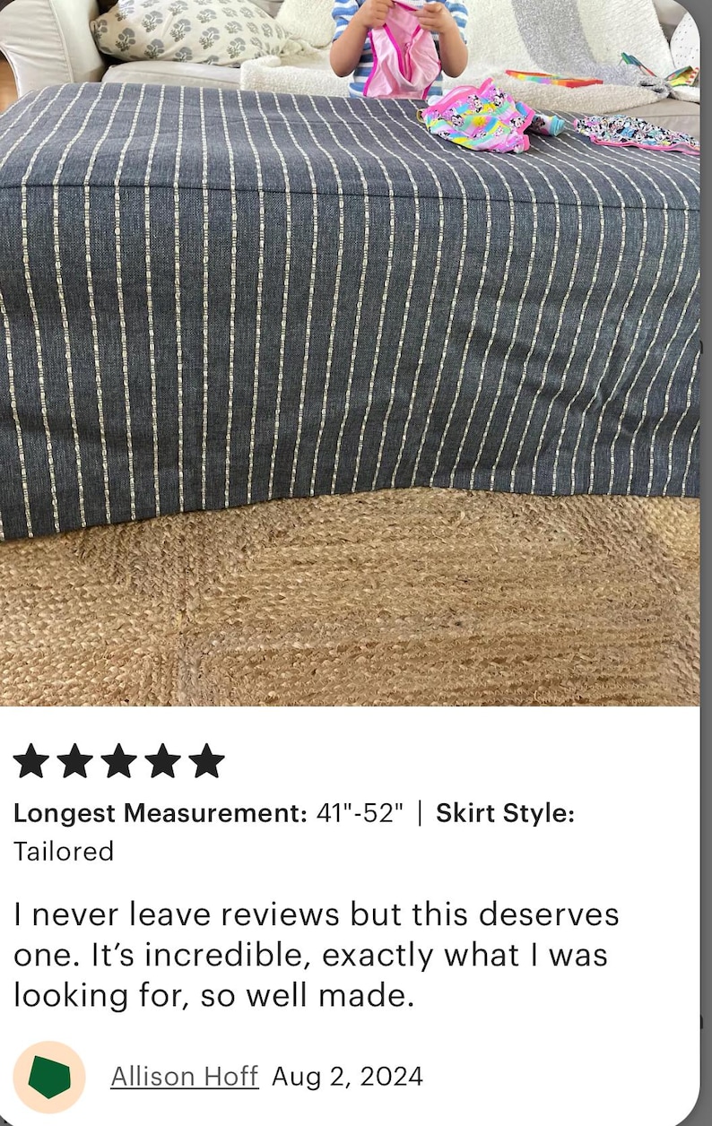 May include: A large, rectangular ottoman with a dark gray fabric cover featuring vertical white stripes. The ottoman's longest measurement is between 41 and 52 inches. The ottoman is on a woven jute rug.