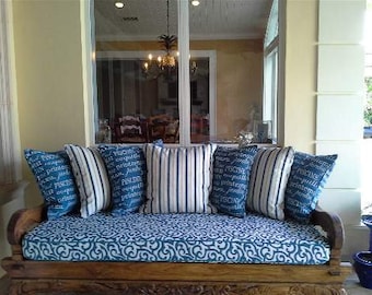 May include: A wooden bench with a blue and white patterned cushion. The bench has a carved design on the front and is placed on a porch with a view of a patio.