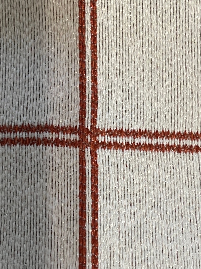 May include: A close-up of a white woven fabric with two brown stripes running vertically and horizontally across the fabric.
