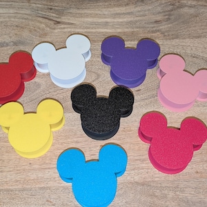 Op de afbeelding: Acht schuimrubberen Mickey Mouse-kopvormige containers in verschillende kleuren: rood, wit, paars, roze, geel, zwart, rood en blauw.