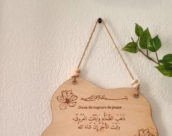 May include: A wooden sign with an Islamic prayer for breaking the fast during Ramadan. The sign is decorated with floral designs and has a rope for hanging. The text on the sign reads: "Dhahaba z-zama u wa btallati-l-'ouroûqou wa thabata-l-ajrou in shâ a l-lâhou. La soif est dissipée, les veines sont abreuvées et la récompense restera avec la volonté d'Allah."