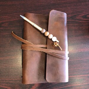 May include: A brown leather journal with a pen and a beaded tassel. The journal is closed and tied with leather straps.