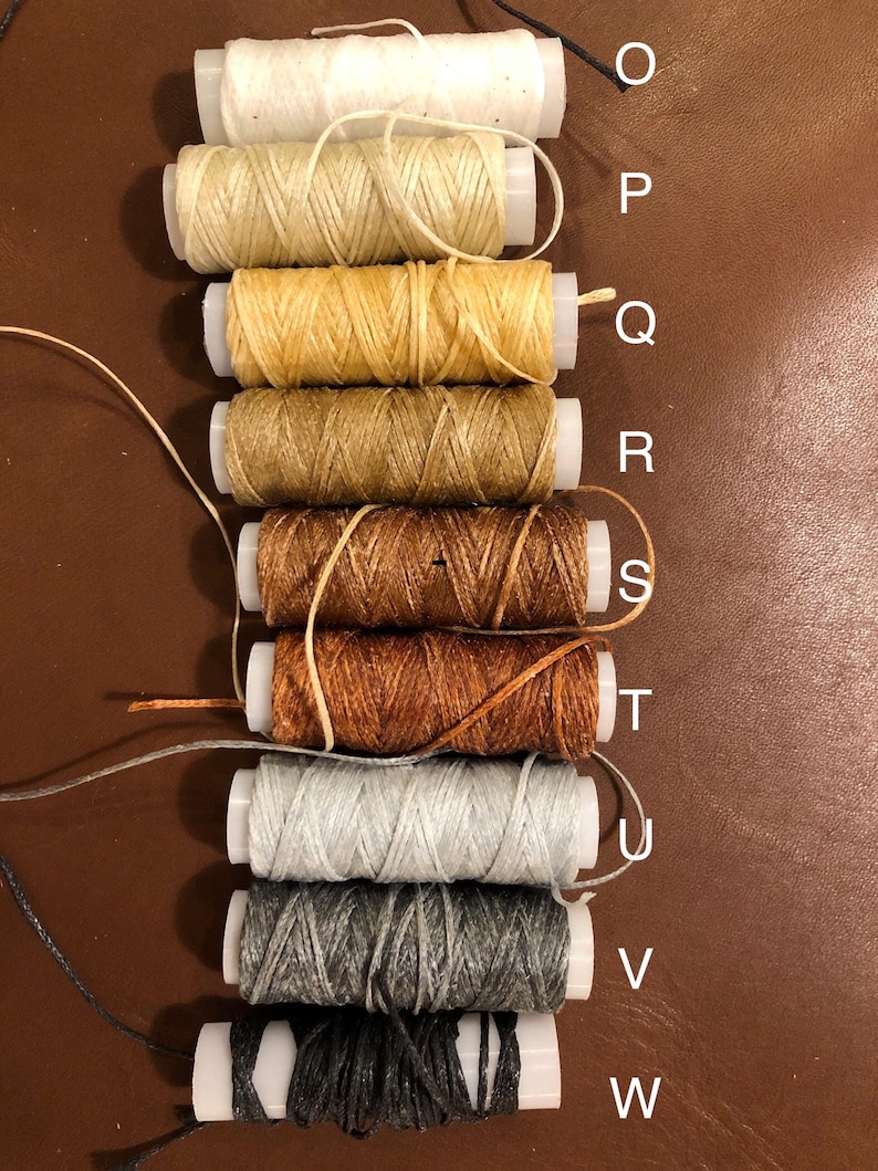 May include: Nine spools of waxed thread in various colors, including white, beige, yellow, brown, orange, gray, and black. The spools are labeled with letters from O to W.