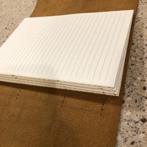 May include: A brown leather-bound journal with lined pages. The journal is open and the pages are visible.