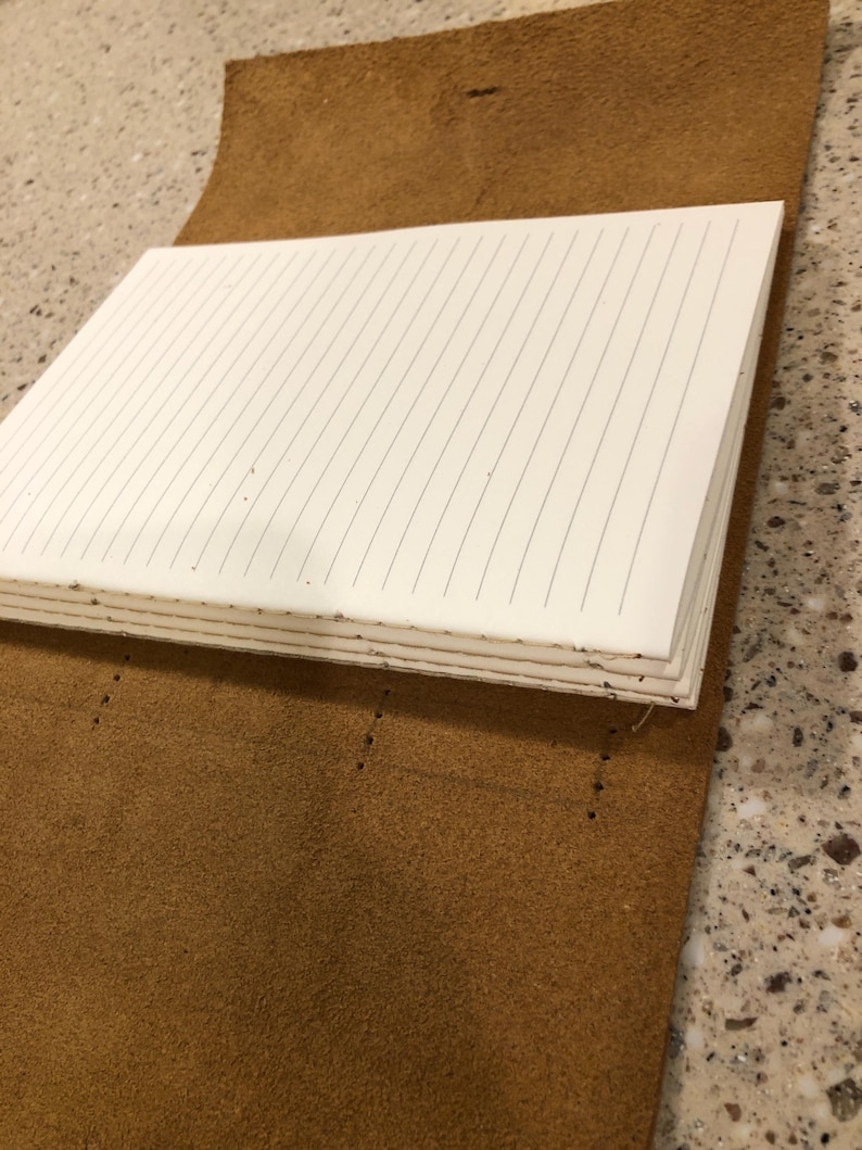 May include: A brown leather-bound journal with lined pages. The journal is open and the pages are visible.