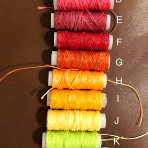 May include: A set of 14 spools of thread in various colors, including purple, red, orange, yellow, green, and blue. The spools are labeled with letters from A to N.