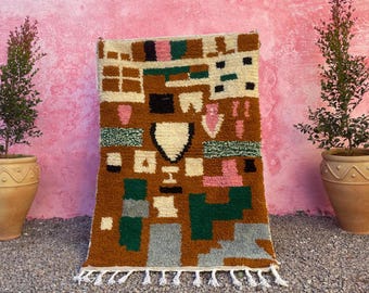 May include: A colorful geometric rug with a brown, white, green, pink, and gray pattern. The rug has a fringe border.