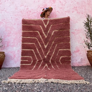 May include: A pink and cream patterned rug with a geometric design. The rug has a fringe border and is laid out on a pink and gray surface.