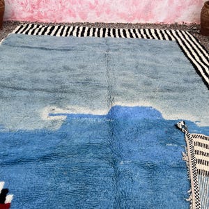 May include: A large, rectangular rug with a blue and white design. The rug has a textured surface and a border of black and white stripes. The rug's design includes a lighter blue shape in the center.