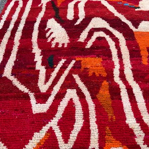 May include: A close-up of a red and white patterned rug. The rug has a textured surface with a repeating pattern of white, wavy lines against a red background. Orange and green accents are also visible.