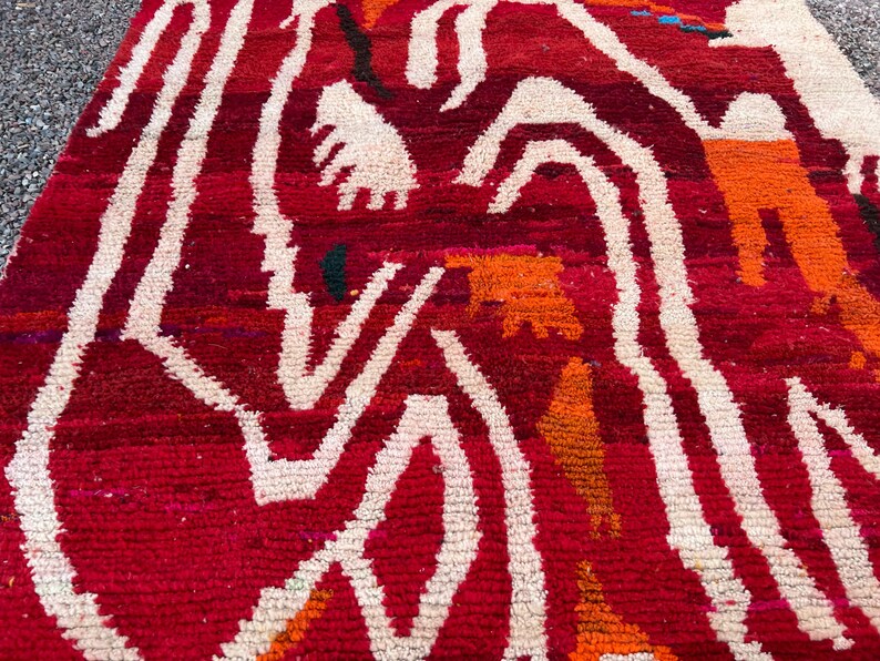May include: A close-up of a red and white patterned rug. The rug has a textured surface with a repeating pattern of white, wavy lines against a red background. Orange and green accents are also visible.