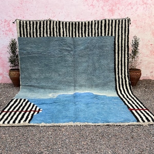 May include: A large, rectangular rug with a blue and white design. The rug has a black and white striped border and a blue center with a lighter blue section at the bottom. Red accents are visible.