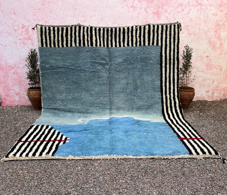 May include: A large, rectangular rug with a blue and white design. The rug has a black and white striped border and a blue center with a lighter blue section at the bottom. Red accents are visible.