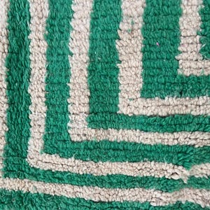 Pode incluir: Close-up de um tapete texturizado com um padr&atilde;o repetido de grossas listras verdes verticais alternadas com listras esbranqui&ccedil;adas. O design do tapete apresenta um canto geom&eacute;trico.