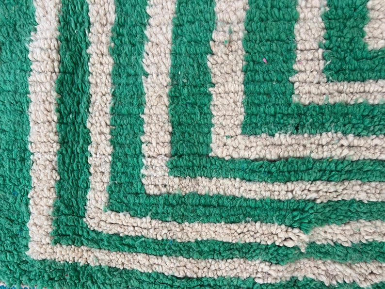 Pode incluir: Close-up de um tapete texturizado com um padr&atilde;o repetido de grossas listras verdes verticais alternadas com listras esbranqui&ccedil;adas. O design do tapete apresenta um canto geom&eacute;trico.