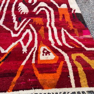 May include: A vibrant, hand-woven rug with a geometric design. The rug features a rich red background with white, orange, and yellow abstract patterns. The edges are finished with a white fringe. This rug is suitable for home decor.