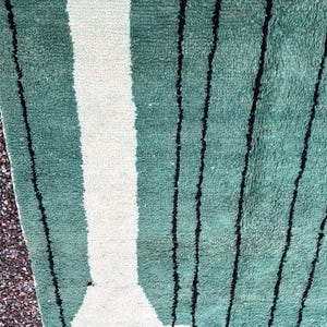 May include: Close-up of a green and white striped rug with black vertical lines. The rug has a textured surface and a geometric design. The rug is made of a soft material and is suitable for home decor.