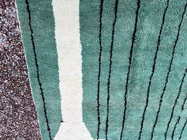 May include: Close-up of a green and white striped rug with black vertical lines. The rug has a textured surface and a geometric design. The rug is made of a soft material and is suitable for home decor.