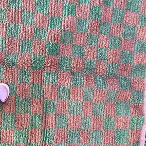 May include: A green and brown checkered rug with a fuzzy texture. The rug is made of woven fabric and has a square shape.