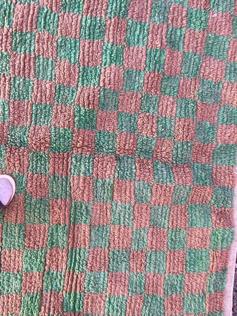 May include: A green and brown checkered rug with a fuzzy texture. The rug is made of woven fabric and has a square shape.