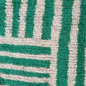 Pode incluir: Close-up de um tapete texturizado com um padr&atilde;o repetitivo de listras verdes verticais alternando com listras bege. O design do tapete tamb&eacute;m apresenta listras verdes horizontais, criando um padr&atilde;o geom&eacute;trico. O tapete tem uma apar&ecirc;ncia macia e felpuda.