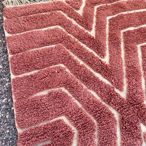 May include: A pink and white geometric patterned rug with a fluffy texture. The rug has a chevron pattern with white lines on a pink background.