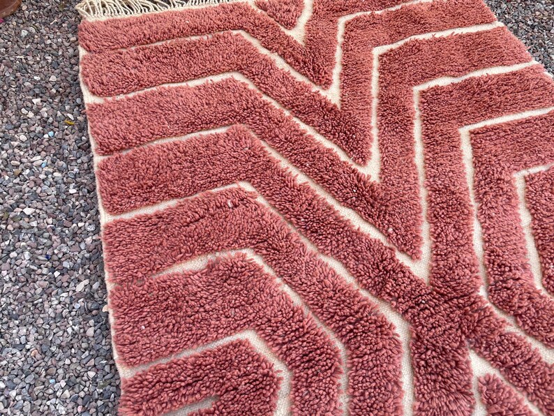 May include: A pink and white geometric patterned rug with a fluffy texture. The rug has a chevron pattern with white lines on a pink background.
