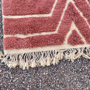 May include: A pink and white geometric patterned rug with a fringe border. The rug is made of a soft, fluffy material.