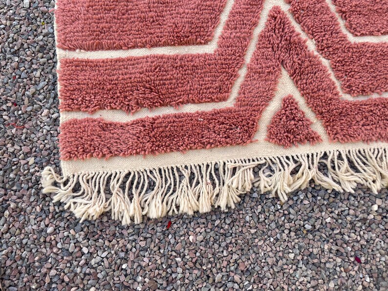 May include: A pink and white geometric patterned rug with a fringe border. The rug is made of a soft, fluffy material.