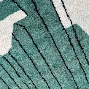 May include: Close-up of a textured rug with a geometric design. The rug features a teal green color with black stripes and white shapes. The rug has a soft, plush appearance.