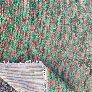 May include: A green and brown checkered rug with a fringe border. The rug is made of a soft, fluffy material and has a woven backing.