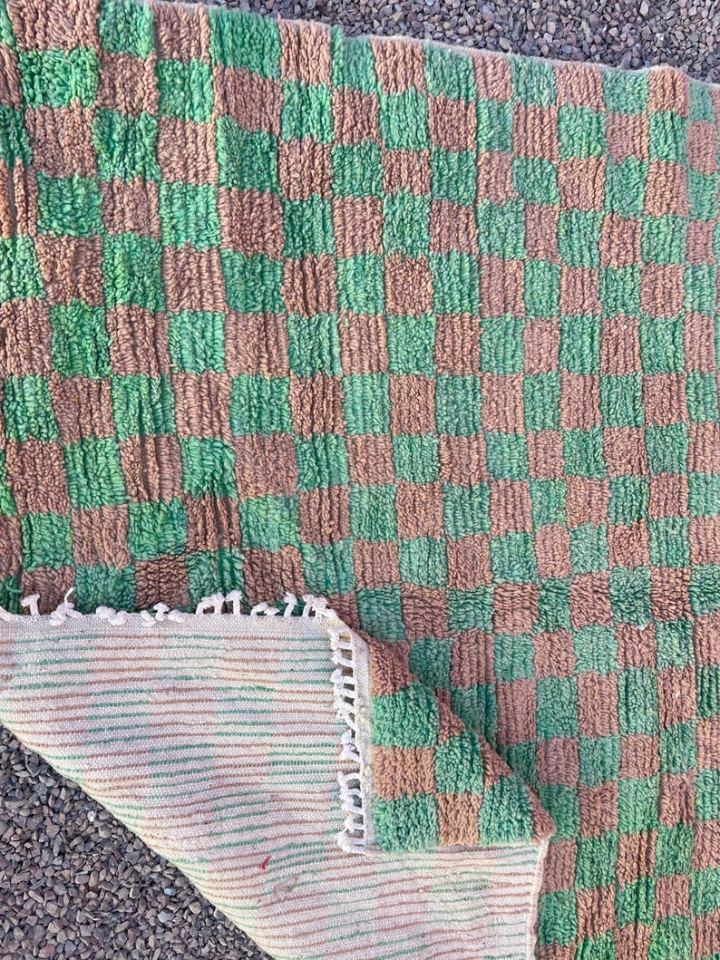 May include: A green and brown checkered rug with a fringe border. The rug is made of a soft, fluffy material and has a woven backing.