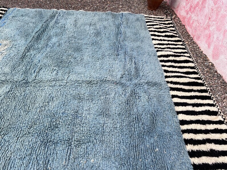 May include: A rectangular rug with a light blue, textured center and a black and white striped border. The rug has a soft, plush appearance, suitable for a living room or bedroom. The rug's dimensions are not visible.