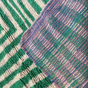 Pode incluir: Close-up de dois tapetes texturizados. Um tapete apresenta um padr&atilde;o em zigue-zague verde e creme. O outro tapete tem um padr&atilde;o de listras diagonais em tons de azul, verde e rosa. Os tapetes parecem ser feitos de um material espesso e tecido.