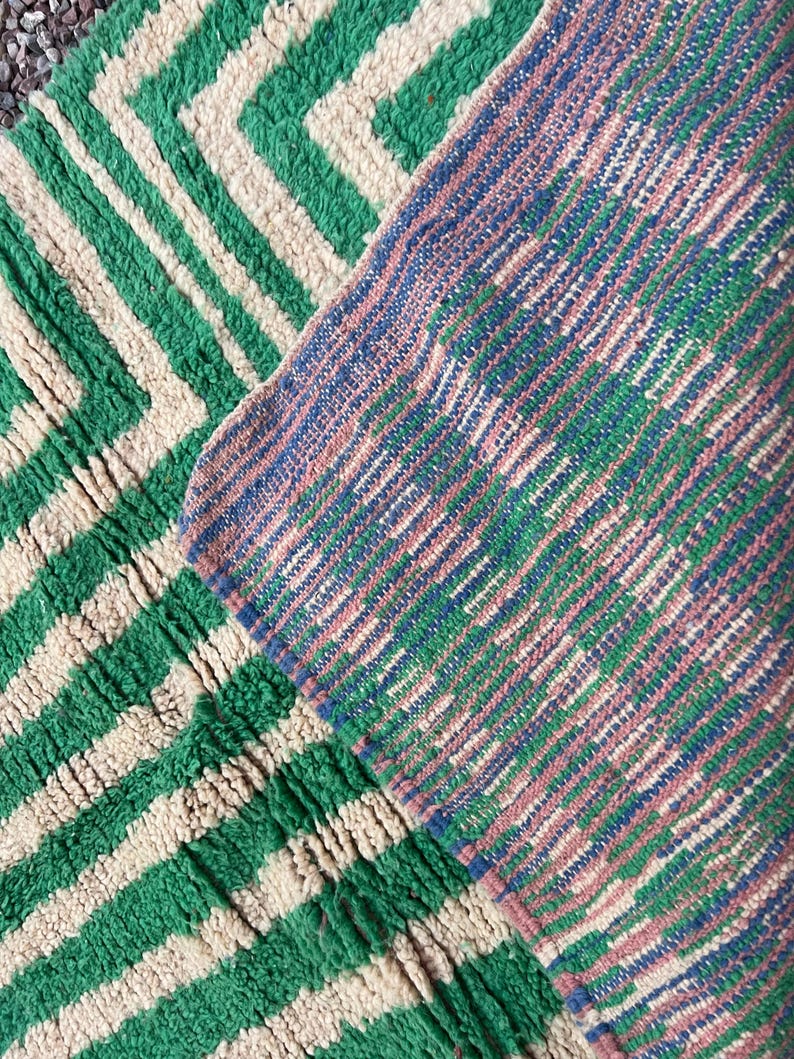 Pode incluir: Close-up de dois tapetes texturizados. Um tapete apresenta um padr&atilde;o em zigue-zague verde e creme. O outro tapete tem um padr&atilde;o de listras diagonais em tons de azul, verde e rosa. Os tapetes parecem ser feitos de um material espesso e tecido.