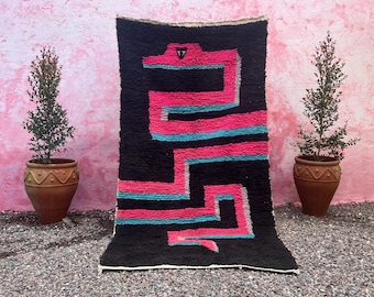 Könnte beinhalten: Ein schwarz-weißer Teppich mit einem geometrischen Muster in Pink und Blau. Der Teppich hat einen Fransenrand und ist aus Wolle.