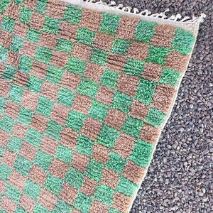 May include: A green and brown checkered rug with a fringe border. The rug is made of a soft, fluffy material.