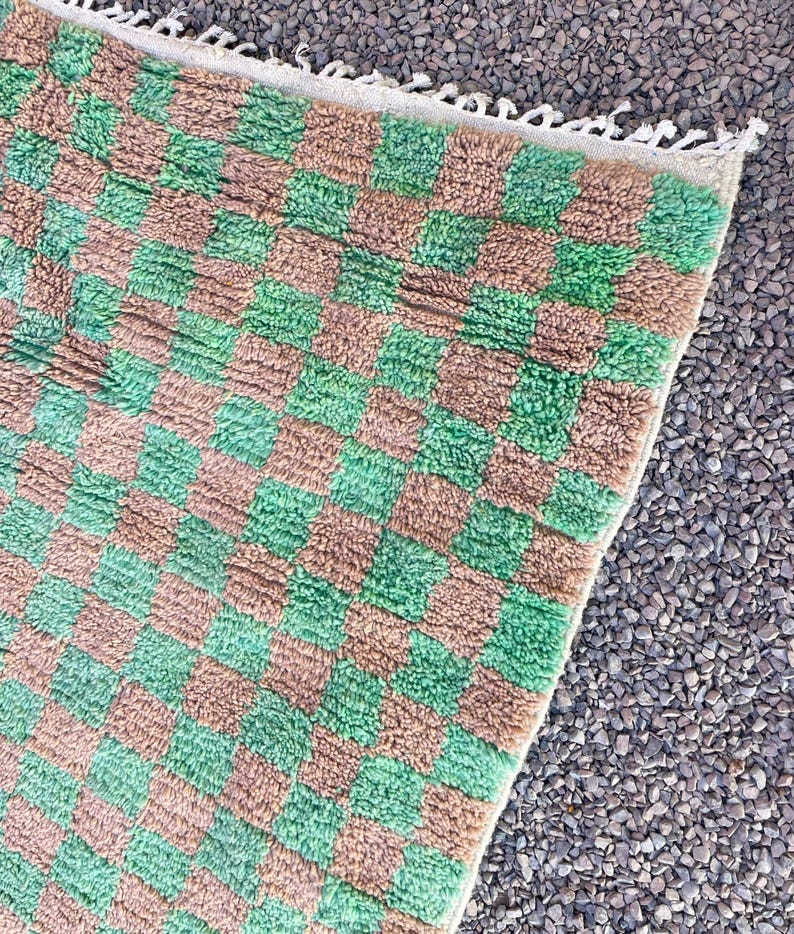 May include: A green and brown checkered rug with a fringe border. The rug is made of a soft, fluffy material.