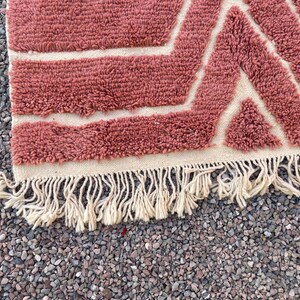 May include: A pink and white geometric patterned rug with a fringe border. The rug is made of a soft, fluffy material.