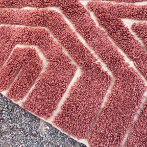 May include: A close-up of a pink and white bath mat with a geometric pattern. The mat is made of a soft, fluffy material.