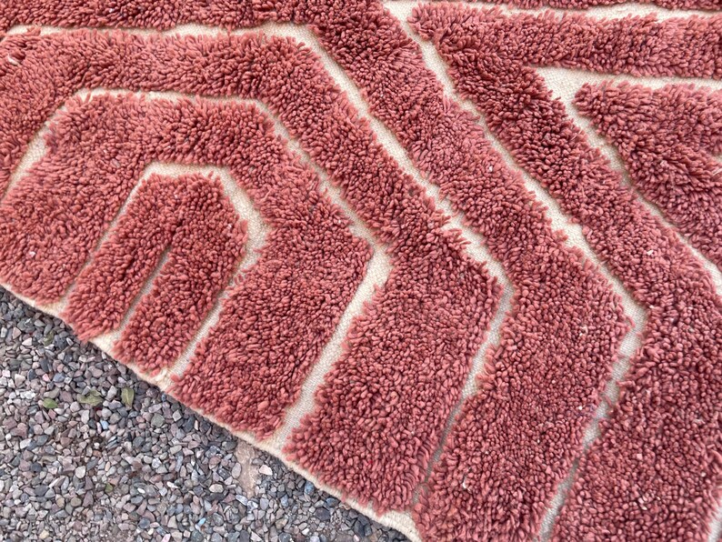 May include: A close-up of a pink and white bath mat with a geometric pattern. The mat is made of a soft, fluffy material.